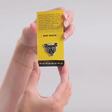 Hands opening matchbox-style packaging with enamel pin inside