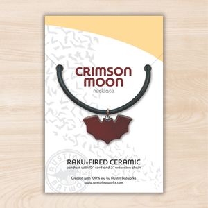 Crimson Moon necklace packaging with a ceramic pendant on a light wood background