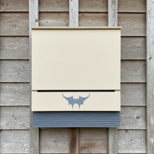 large single chambered bat house painted light tan on rustic wood background
